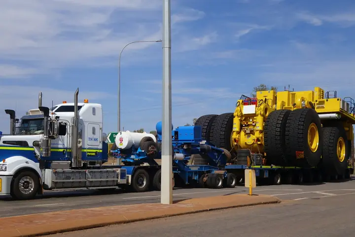 Heavy-haul tractor unit and low-loader trailer carrying an oversized yellow mining dump truck