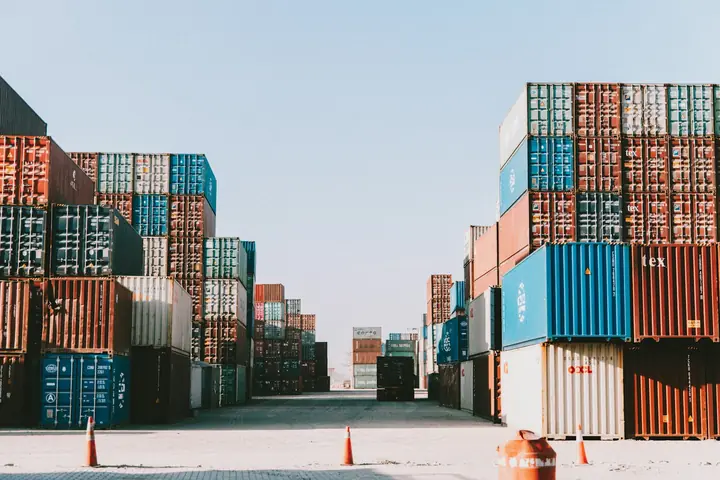 Rows of stacked shipping containers in a container yard under a pale sky