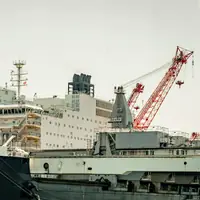 A large offshore construction vessel alongside, with its accommodation block and a red crane
