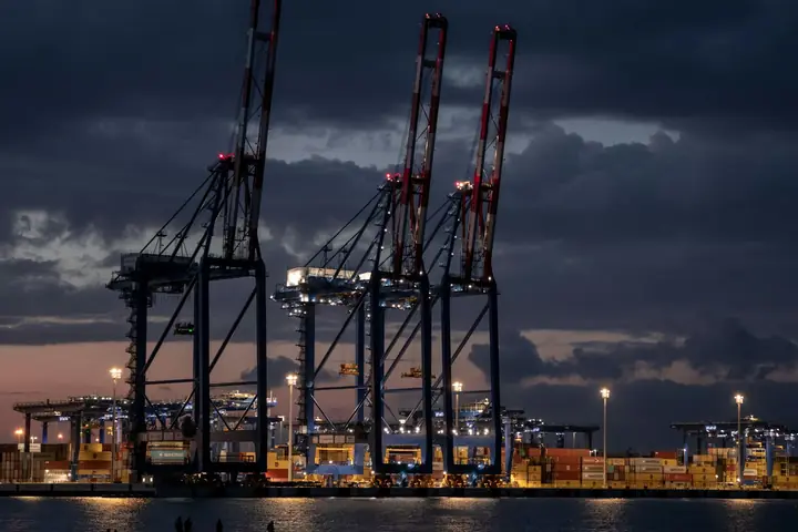 Ship-to-shore container cranes silhouetted against the evening sky at a port