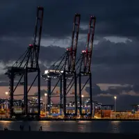 Ship-to-shore container cranes silhouetted against a dark evening sky at a port