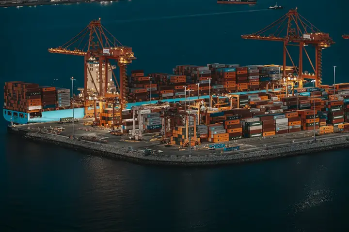 Aerial view of a container terminal with cranes and stacked boxes beside deep blue water