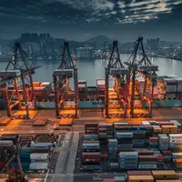 Container terminal at dusk with ship-to-shore cranes working a container ship under a dramatic sky