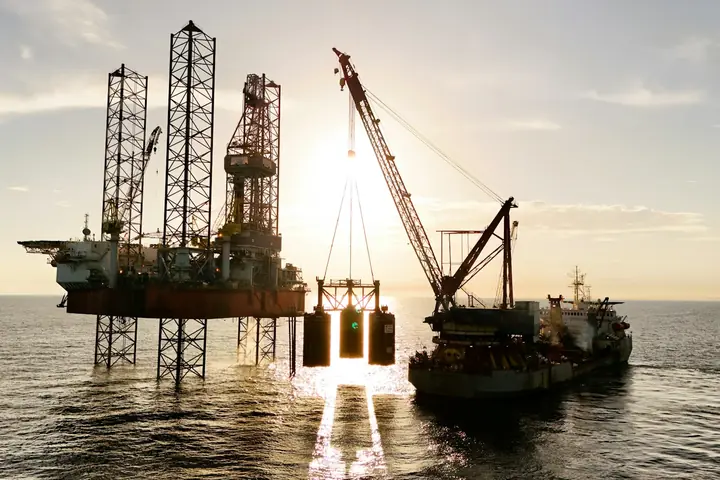 A jack-up rig and a crane vessel silhouetted against the setting sun at sea