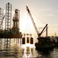 A jack-up rig and a crane vessel silhouetted against the setting sun at sea